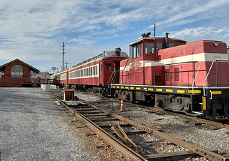 A red and white train on the tracks near a building. Middletown & Hummelstown Railroad.